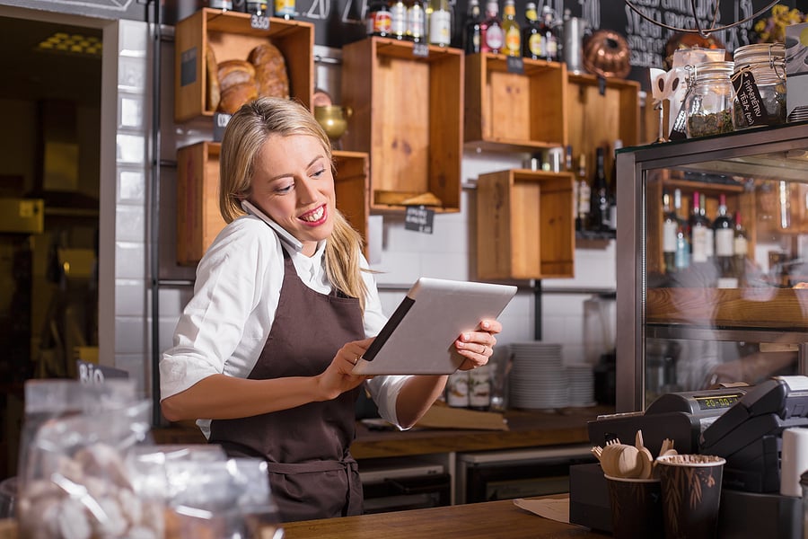 Cafe owner reviewing orders on a tablet behind the counter
