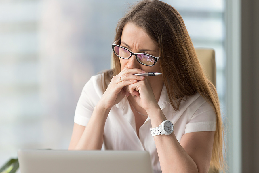 Woman thinking with a pen at her mouth in front of a laptop
