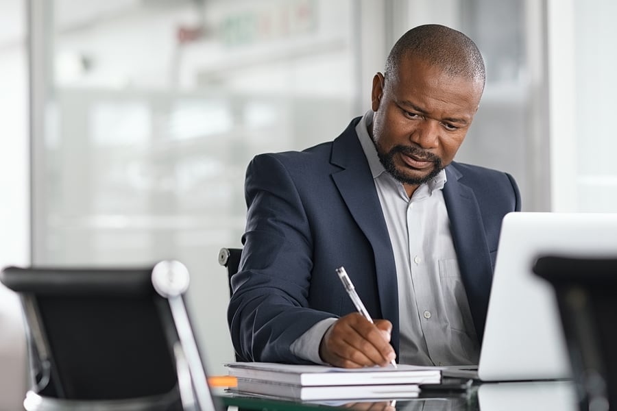 Businessman writing notes at his desk with a laptop