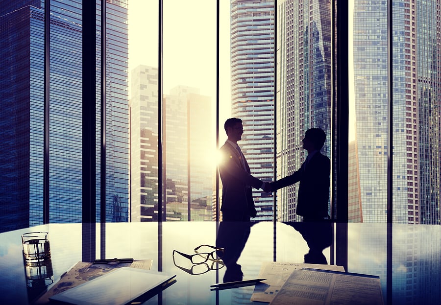 Silhouetted business handshake in front of city skyscraper windows