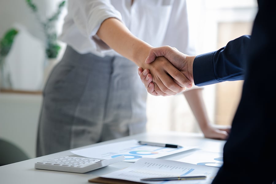 Two professionals shaking hands over financial documents and a calculator