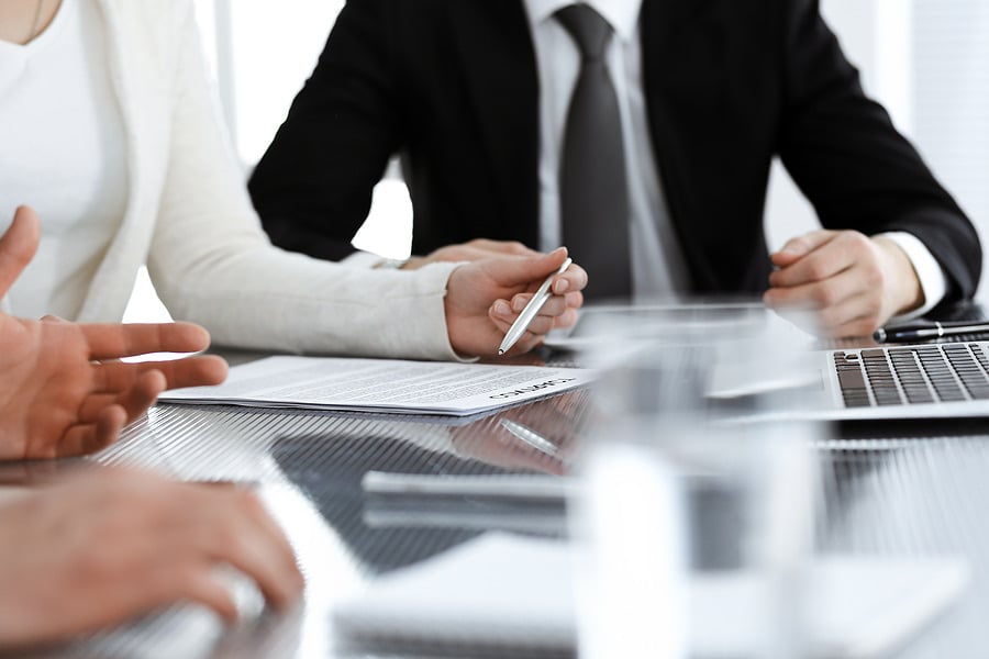 Businessman with pen and paperwork discussing terms near a laptop
