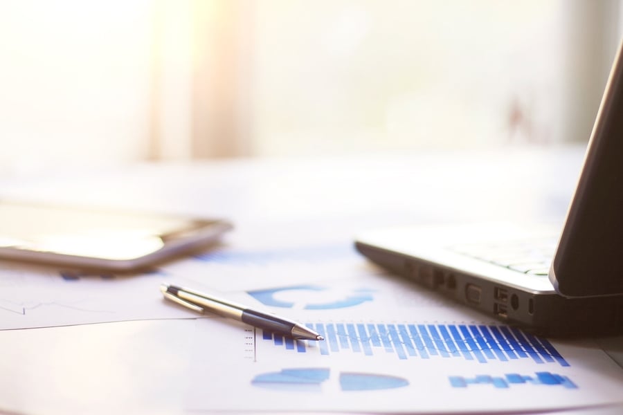 Pen resting on a printed chart beside a tablet and laptop
