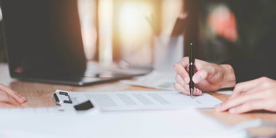 Hand signing a document with a laptop on the desk