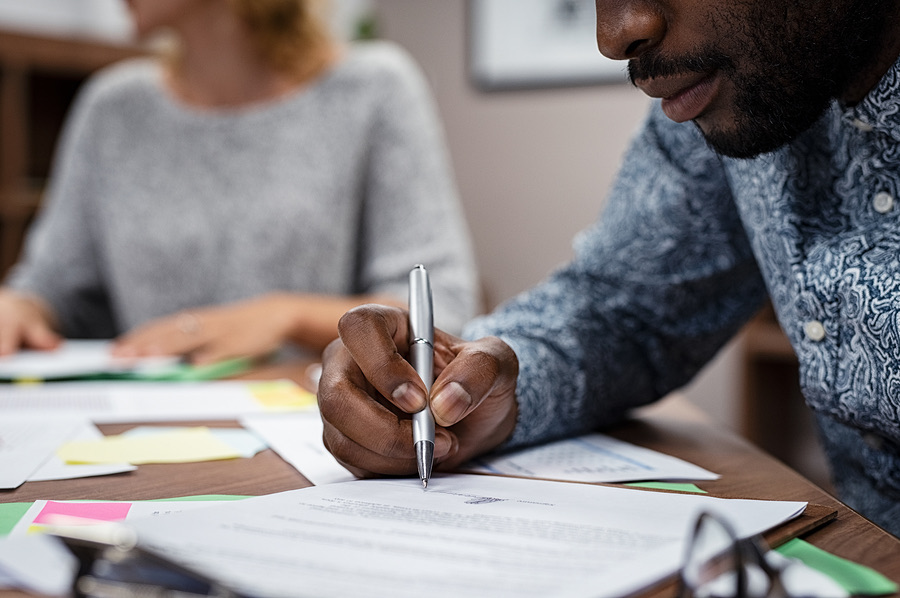 Hand signing a document at a desk with sticky notes