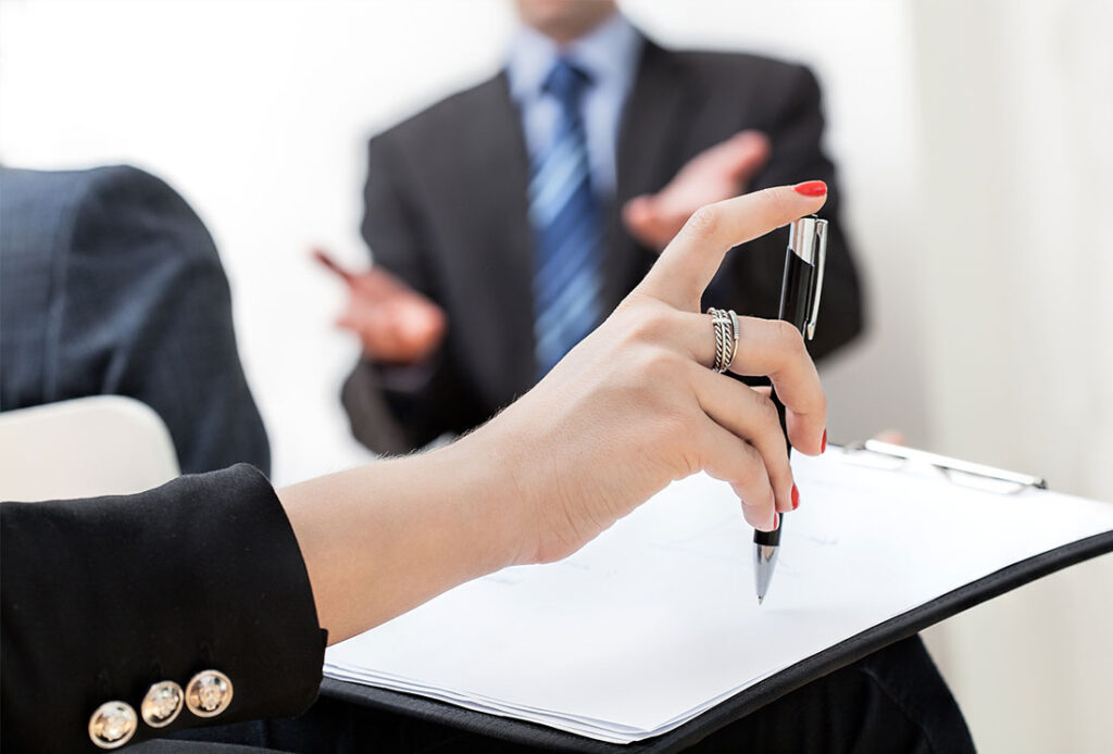 Person signing a document while a colleague gestures nearby
