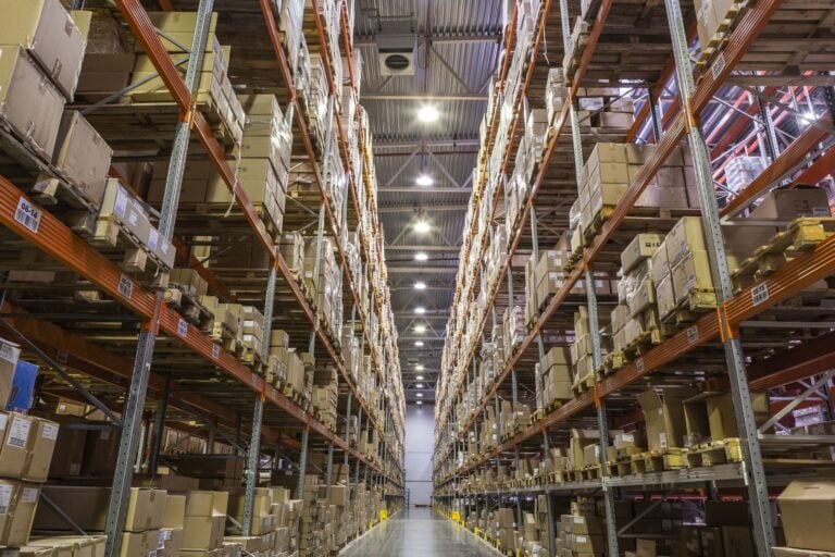 Long aisle of a distribution warehouse lined with stocked shelves