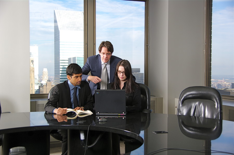 Three colleagues reviewing a laptop in a high-rise conference room