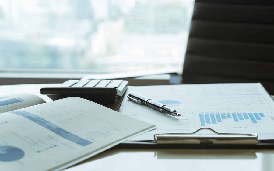 Pen resting on financial charts beside a calculator on a desk