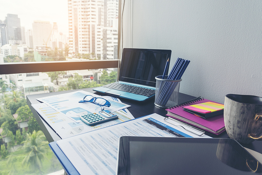 Desk with laptop, financial charts and calculator by a city window