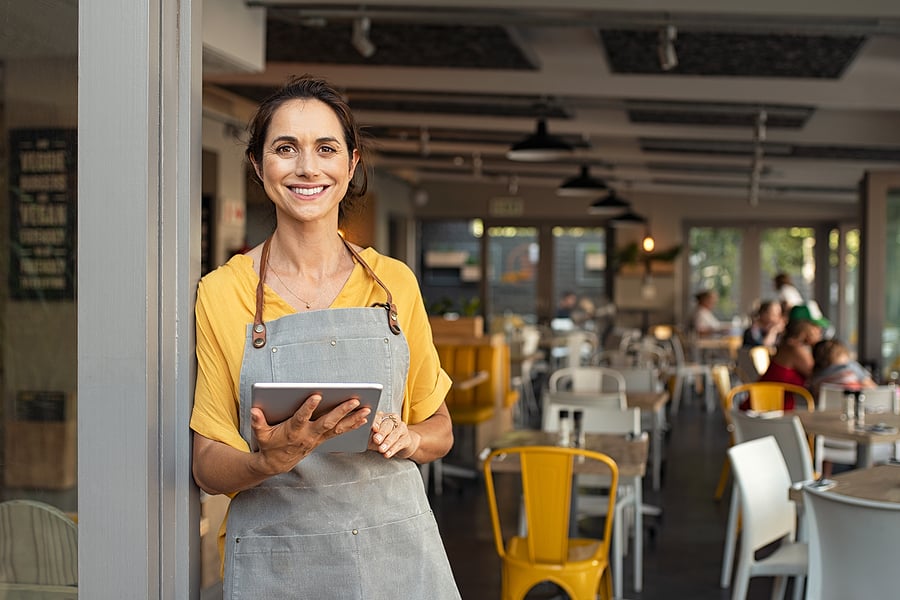 Restaurant owner holding a tablet and smiling in her dining room
