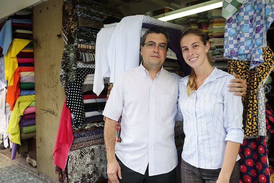 Father and daughter smiling together inside their fabric shop