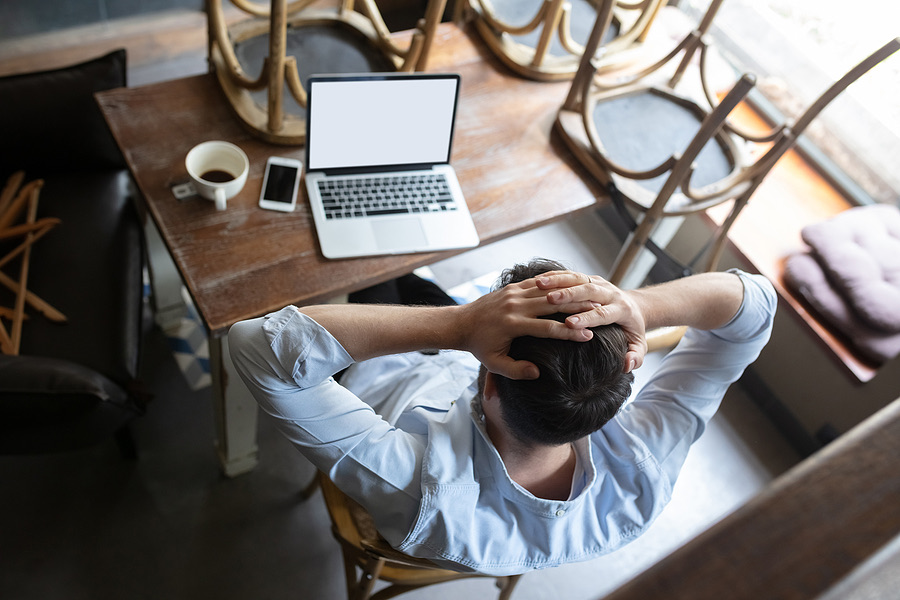 Stressed man holding his head at a cafe table with a laptop