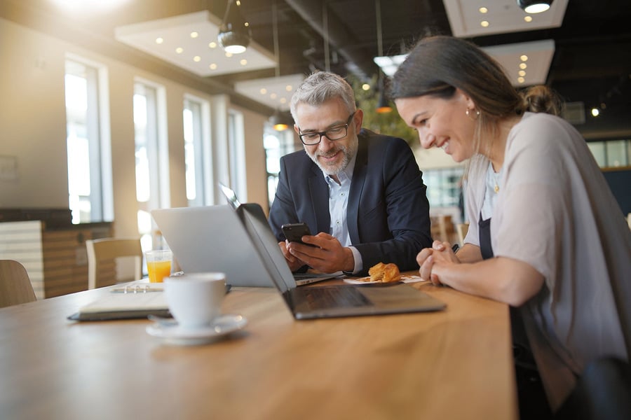 Two colleagues reviewing a phone together at a cafe table