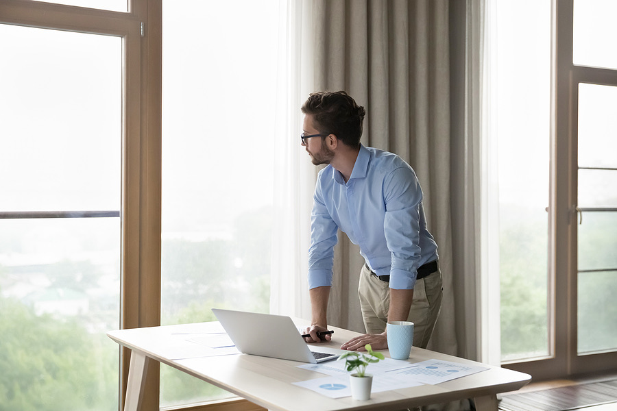 Man reviewing a laptop while standing at a window desk