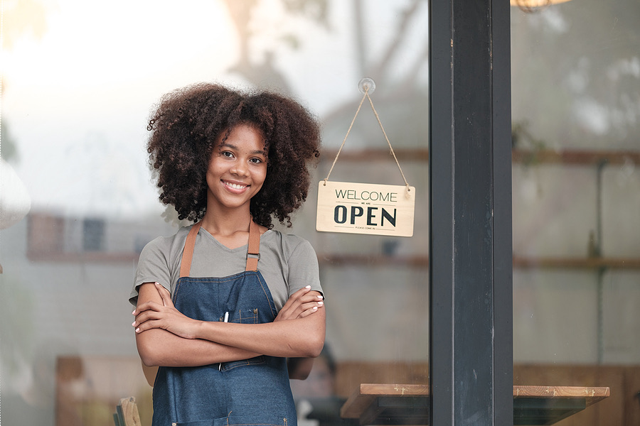 Shop owner smiling with arms crossed beside a welcome sign