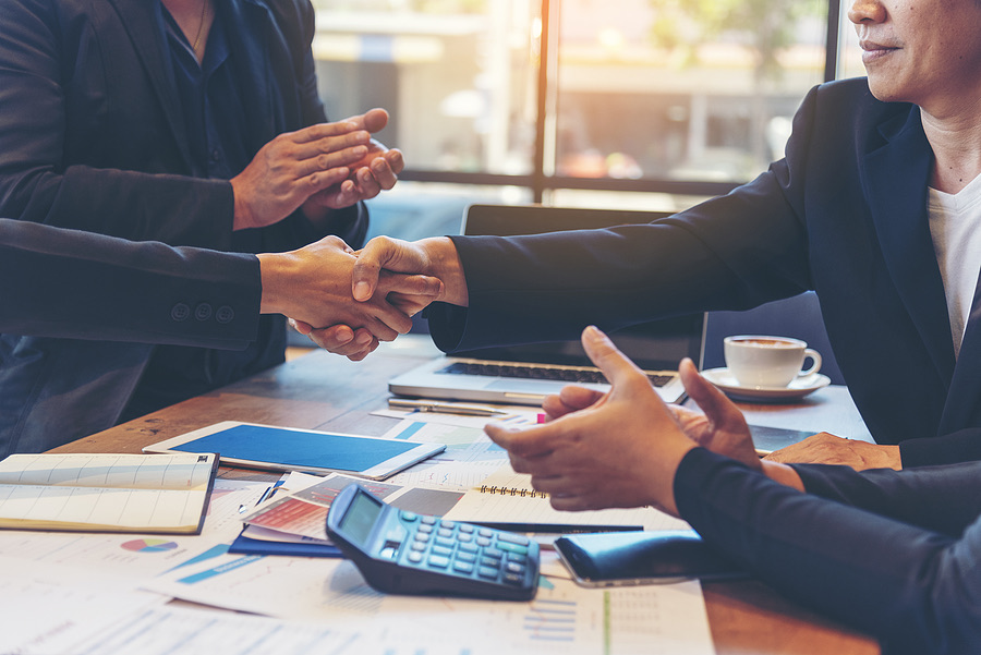 Two professionals shaking hands over financial documents during a meeting