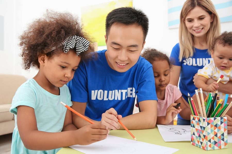 Volunteers in branded shirts helping a child with an activity